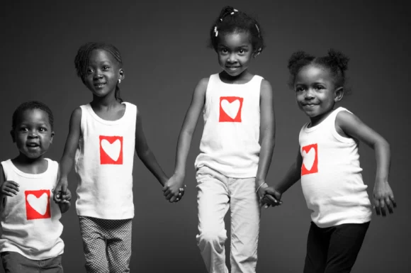 Four children holding hands wearing heart-logo shirts, symbolizing unity and pediatric heart surgery support.