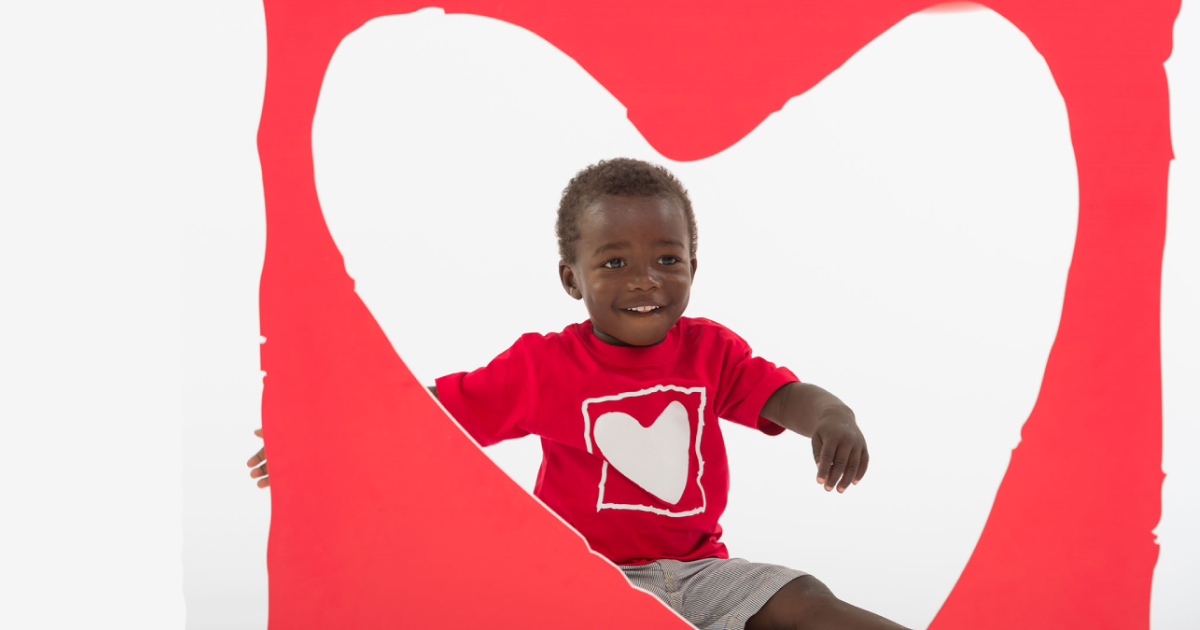Child smiling inside a heart cut-out, representing children supported by cardiac surgery programs.